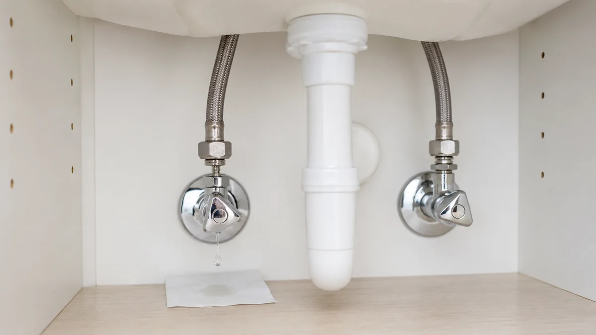 Einzelner Wassertropfen an einem Armaturen-Flexschlauch mit Prüfpapier unter dem Waschbecken.